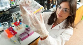 Woman in Lab Coat and Safety Glasses Views Lab Samples
